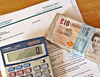paper tax return form with a calculator and ten pound notes