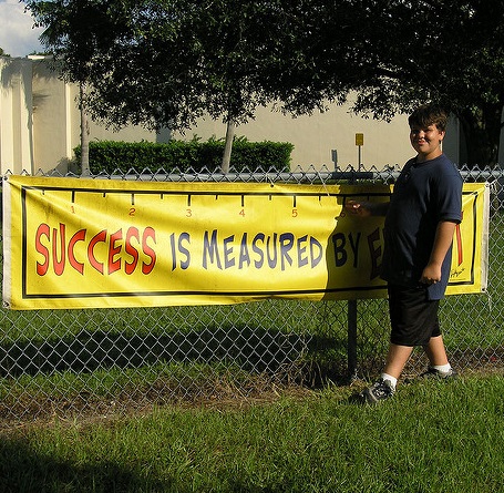 boy standing in front of a banner reading 'success is measured by...'The final word is obscured