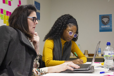 one woman making notes while another is using a laptop to try out a service