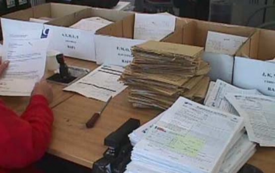 desk piled high with forms and cardboard boxes for sorting them into