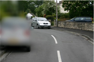 view of car coming along road with object on left hand side of vision indistinguishable