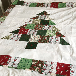 A quilt top on a bed. There are squares and traingles of Christmas fabrics making the shape of a Christmas tree