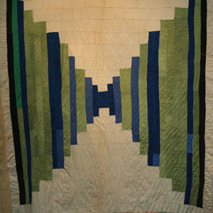 A quilt in a geometric design made from strips of blue and green fabric at the sides, with cream fabric top and bottom. The strips are tiny in the middle and increase to the edges.
