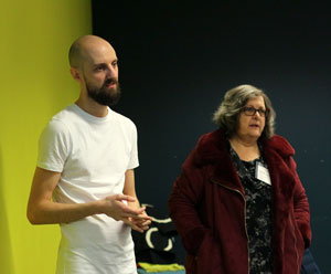 A tall man in a white shirt stands next to a short woman wearing a burgundy coat