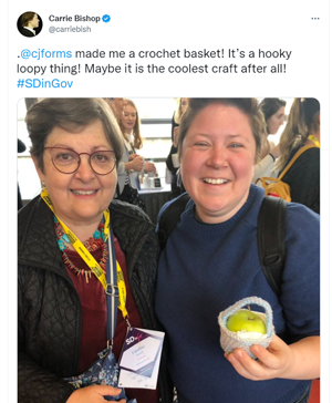A tweet from Carrie Bishop featuring a photograph of her holding a crochet basket just big enough to hold an apple, next to Caroline Jarrett wearing a conference lanyard.