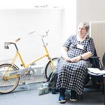 A yellow bicycle nex to a window, with a woman in a black and white checked dress sitting next to it.