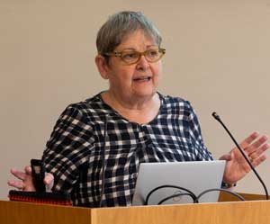 Caroline speaking at a conference. She's an older white woman wearing glasses. 